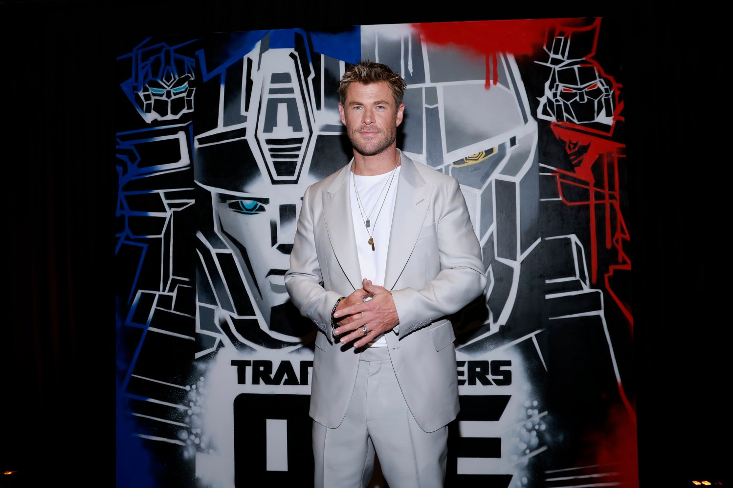 Chris Hemsworth pose devant un arrière-plan mettant en vedette le film Transformers One
